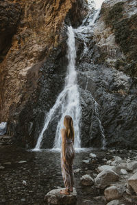 Rear view of woman standing against waterfall