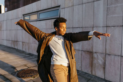 Young man with arms outstretched standing on footpath