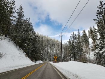 Snow covered road amidst trees against sky