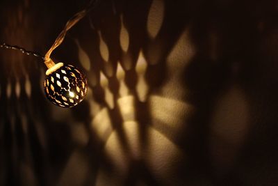 Close-up of illuminated string light with shadow on wall