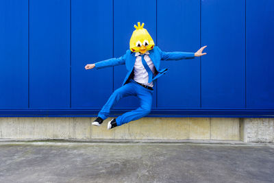 Full length of man jumping against blue wall