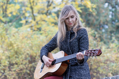 Beautiful young woman playing guitar outdoors