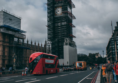 Cars moving on road by buildings against cloudy sky