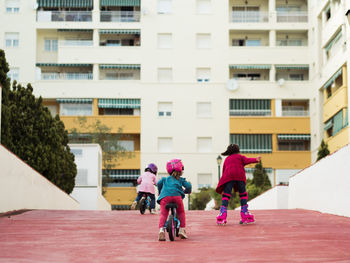 Back view of anonymous little girls on bicycle spending time together near modern apartment building