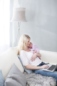 Woman holding newborn daughter and using laptop