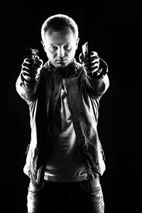 Portrait of man aiming with guns while standing against black background