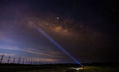 Man holding illuminated flashlight while standing on land against sky at night