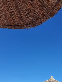 Low angle view of sun umbrella roof against clear blue sky. wood pattern