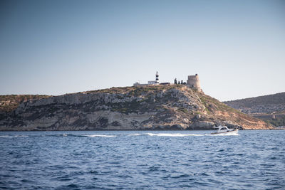 Lighthouse on sea by buildings against clear sky