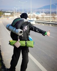 Rear view of backpacker hitchhiking while standing on street