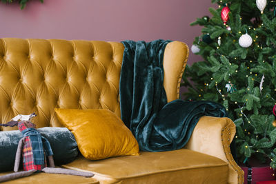 A yellow pillow and an emerald plaid on a yellow vintage sofa near the christmas tree in the living 