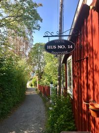 Road sign on street amidst trees against sky