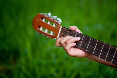 Cropped hand of person playing guitar over field