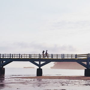 Couple walking on bridge over beach against sky