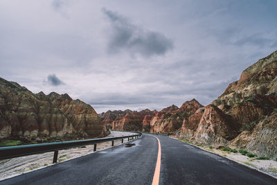 Empty road by mountains against sky