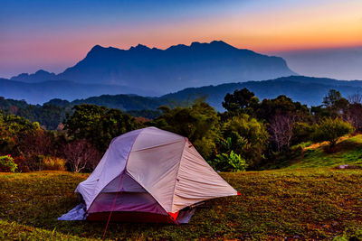 Tent on field by mountains against sky during sunset