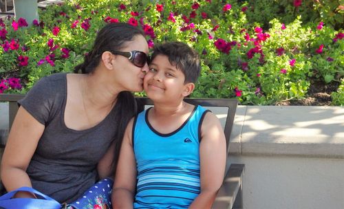 Mother kissing son while sitting on bench at park