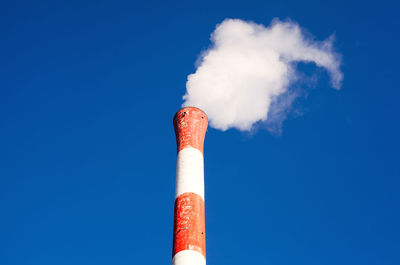 Low angle view of smoke emitting from chimney against blue sky