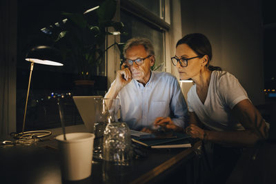 Businesswoman with senior businessman planning strategy in dark office while working late