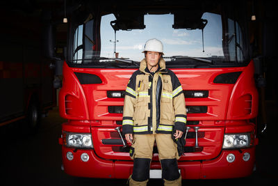 Portrait of female firefighter standing in front of fire engine at fire station