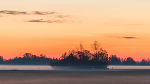 Silhouette trees on landscape against romantic sky at sunset