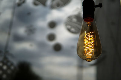 Close-up of illuminated light bulb hanging against wall