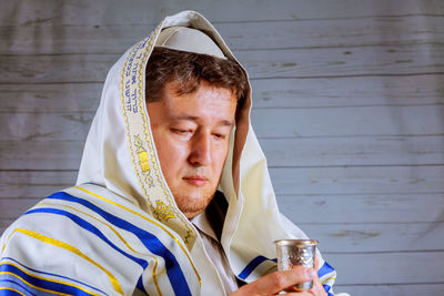 Mature man in jewish prayer shawl holding kiddush cup