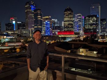 Man standing on a rooftop overlooking the illuminated dallas skyline at night