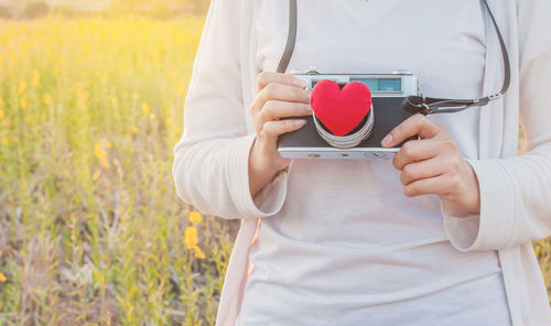 Midsection of woman holding camera with red heart shape
