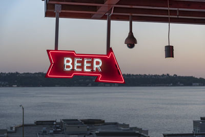 Illuminated signboard hanging against sea