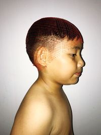 Side view of shirtless boy wearing netting on head against white wall