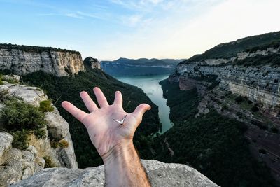 Midsection of person hand on rock at shore against sky