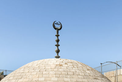 Low angle view of cross against building against clear blue sky