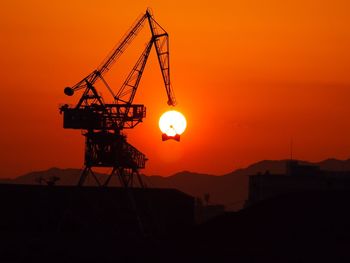 Silhouette cranes at construction site against sky during sunset