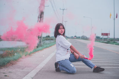 Portrait of young woman holding smoke bomb on road