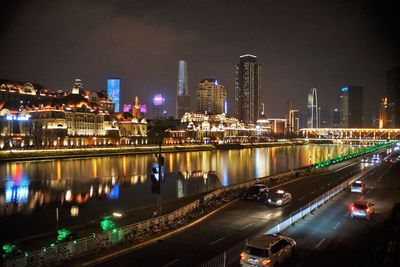 Illuminated city by river against sky at night