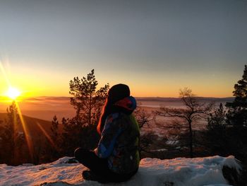 Woman sitting on snow covered cliff during sunset