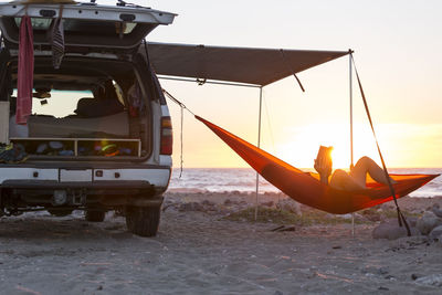 Man relaxing in hammock at beach during sunset