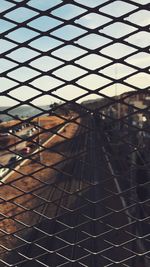 Close-up of metallic fence against sky seen through window