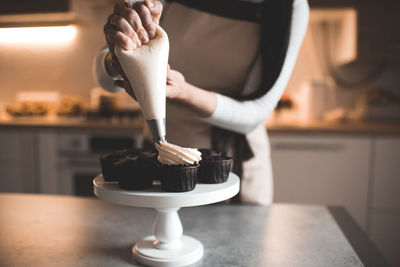 Woman decorate chocolate muffins with whipped cream cheese in kitchen table closeup. working at home