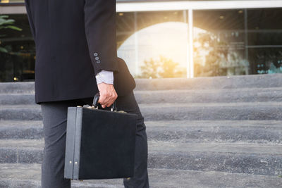 Midsection of businessman standing with briefcase against steps