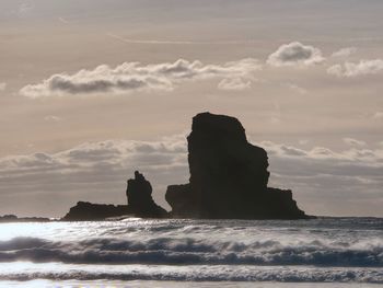 Sharp silhouette of a cliff against the background of sunset. sea waves break on the rocks