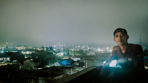 Portrait of man against illuminated buildings in city at night