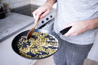 Midsection of man roasting seeds in pan at kitchen