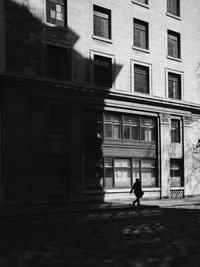 Silhouette person walking on footpath against building