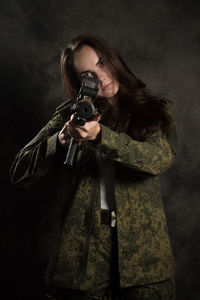 Portrait of woman holding camera while standing against black background