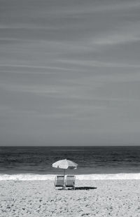 Monochrome image of a air of empty beach chairs with parasol on the sandy beach