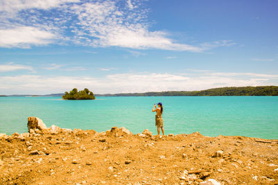 Woman standing on beach against sky photographing with mobile phone