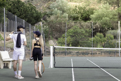 Back view of two friends walking through tennis court about to play a tennis match to be in shape