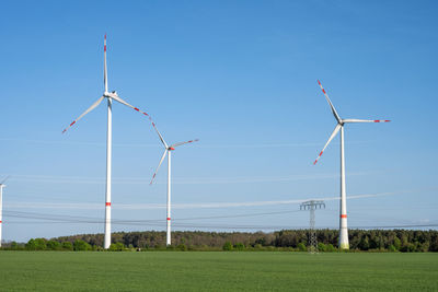 Windmills on field against clear blue sky